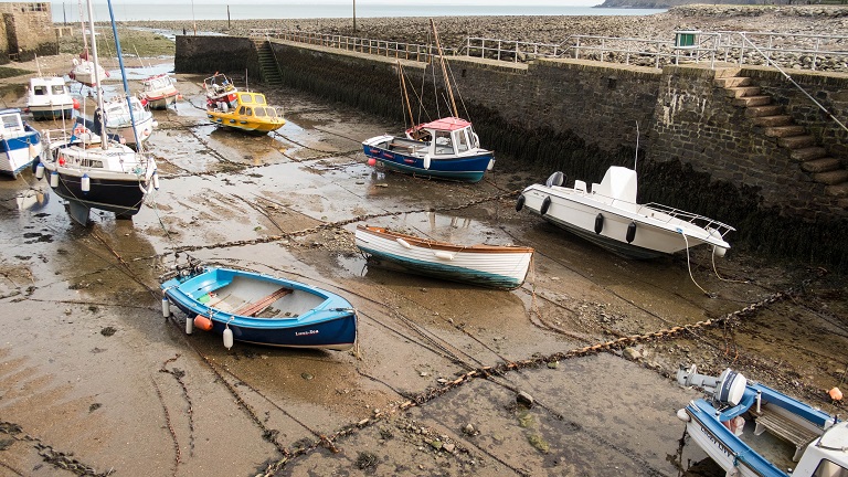 Lynmouth Harbour covered with boats at low tide with Blacklands Beach in the background